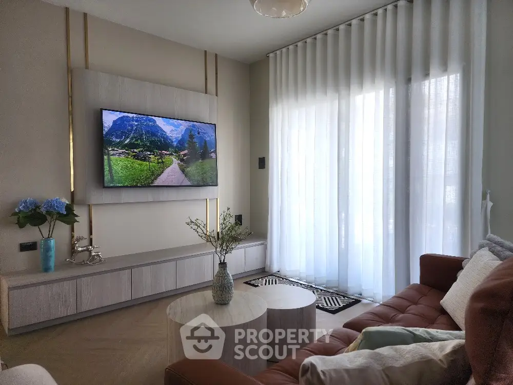 Modern living room with stylish decor and large TV, featuring elegant curtains and cozy seating area.
