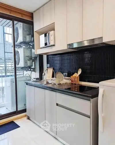 Modern kitchen with sleek cabinetry and balcony view, featuring microwave and ample storage space.