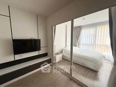 Modern bedroom with sleek design and natural light, featuring a wall-mounted TV and stylish decor.