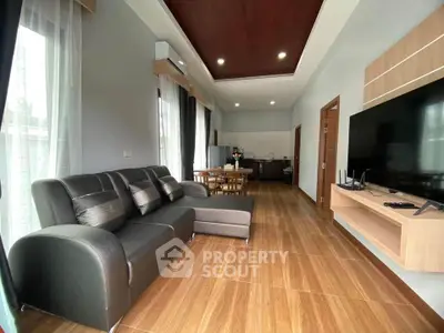 Spacious modern living room with sleek furniture and open kitchen layout, featuring large windows and wooden flooring.
