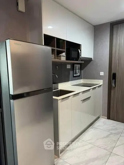 Modern kitchen with sleek cabinetry and stainless steel fridge in a compact layout.