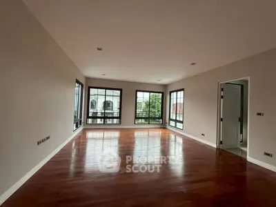Spacious empty room with large windows and wooden flooring, ideal for customization.