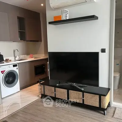 Modern apartment interior with sleek kitchen and cozy living area featuring a washing machine and flat-screen TV.