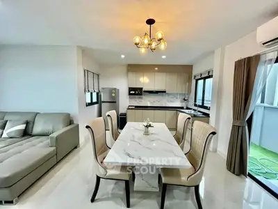 Modern open-layout living and dining area with elegant chandelier and sleek kitchen design.