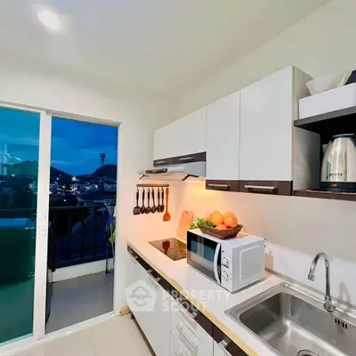 Modern kitchen with sleek cabinets, microwave, and balcony view, perfect for urban living.