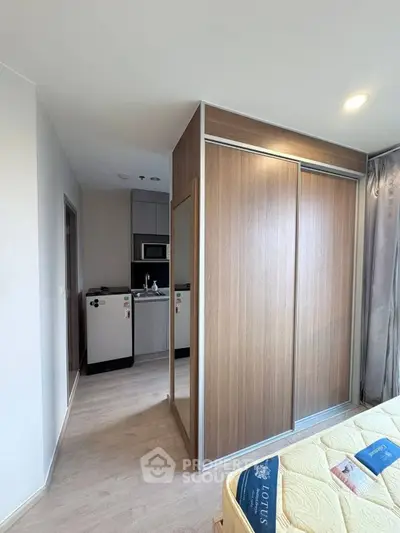 Modern bedroom with built-in wardrobe and compact kitchen area in a stylish apartment.