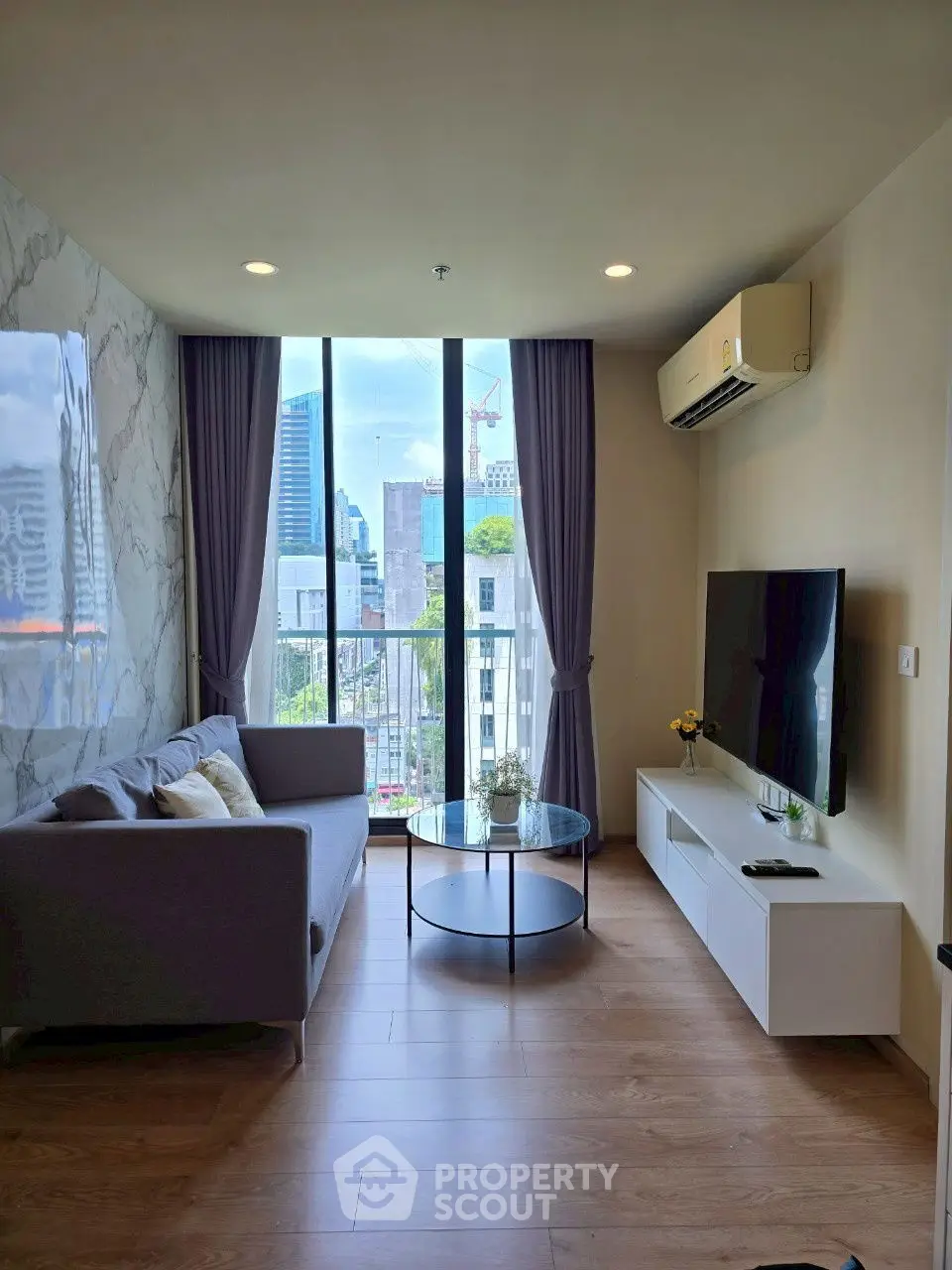 Modern living room with city view, stylish sofa, and sleek TV setup.