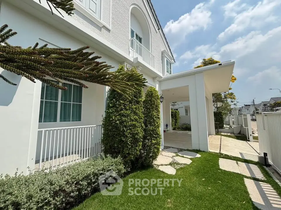 Elegant white house exterior with lush green garden and spacious driveway under clear blue sky.