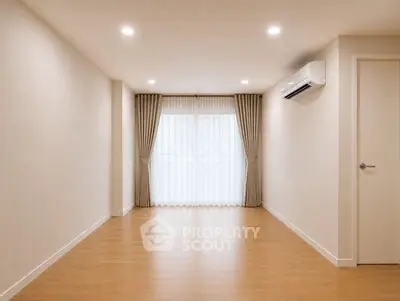 Spacious empty room with wooden flooring and large window, perfect for customization.