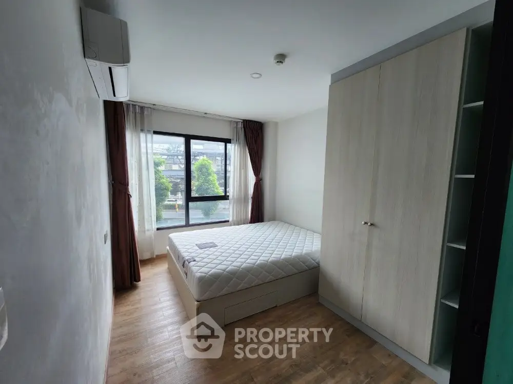 Spacious bedroom with large window and modern furnishings in a bright apartment.