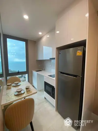 Modern kitchen with ocean view, sleek cabinets, and dining area in a high-rise apartment.