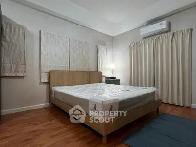 Spacious bedroom with wooden flooring and modern furnishings, featuring a comfortable bed and air conditioning.