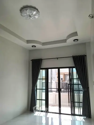 Spacious room with elegant ceiling design and large windows opening to a balcony.