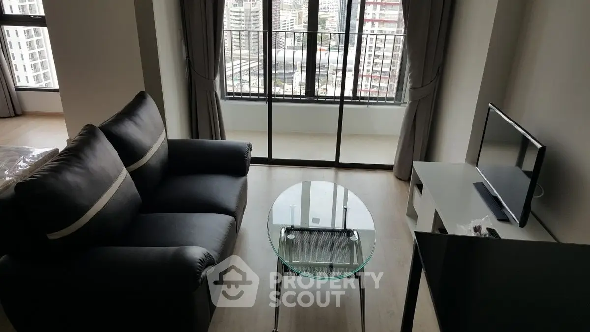 Modern living room with sleek black sofa and glass table, city view from balcony.