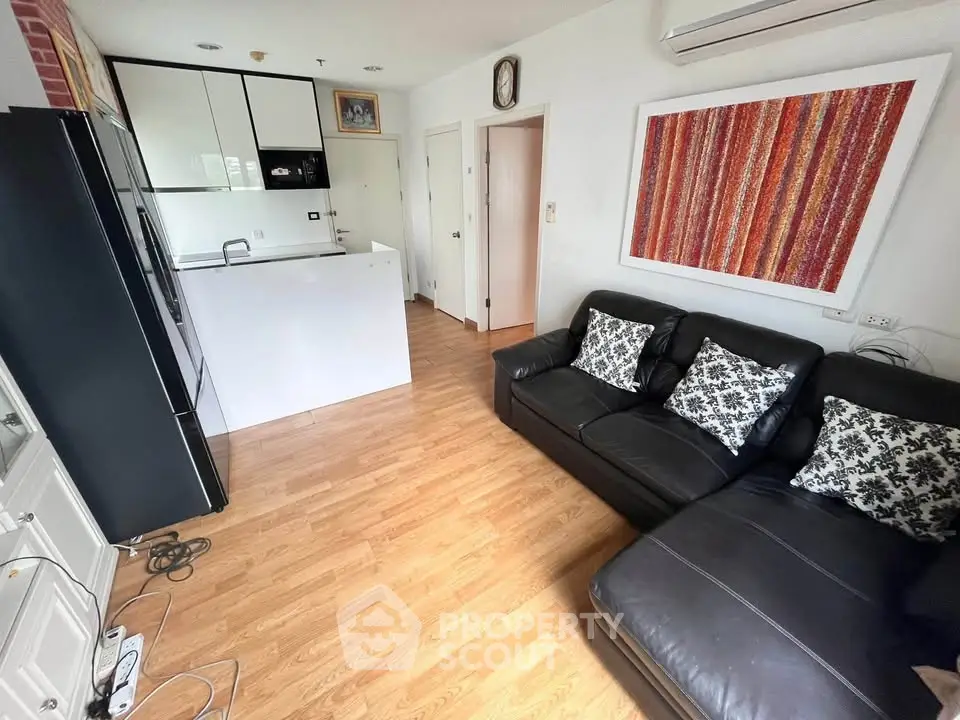 Modern living room with sleek kitchen, black leather sofa, and vibrant wall art in open layout apartment.