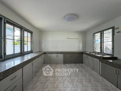 Spacious kitchen with ample counter space and natural light, featuring tiled flooring and modern cabinetry.