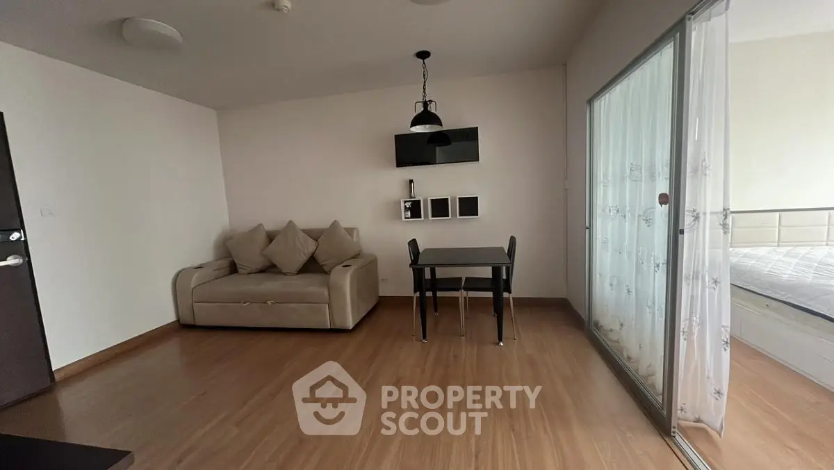 Modern living room with sleek design and cozy sofa, adjacent to a stylish bedroom separated by glass doors.