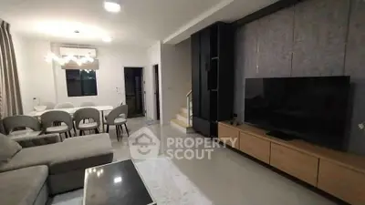 Modern living room with sleek furniture and dining area, featuring a large TV and elegant lighting.