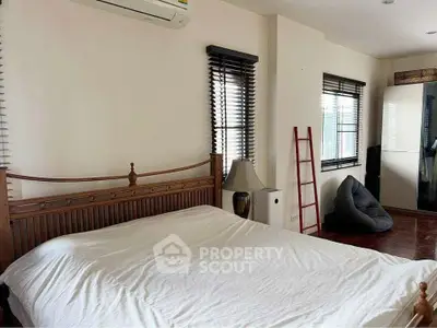 Spacious bedroom with wooden bed frame, air conditioning, and large windows for natural light.