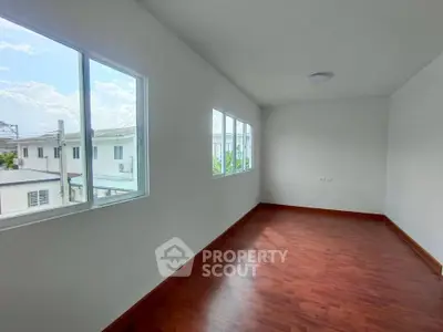 Bright empty room with wooden flooring and large windows offering natural light and neighborhood view.