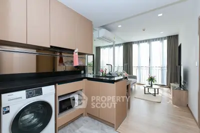 Modern open-layout kitchen with washing machine and cozy living area in stylish apartment.