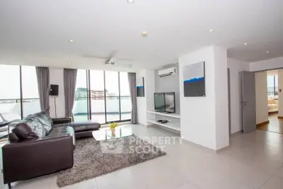 Spacious modern living room with leather sofa and large windows offering city views.