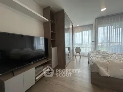 Modern bedroom with large TV and floor-to-ceiling windows offering natural light and scenic views.