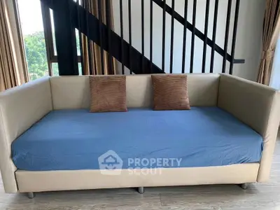 Modern living room with stylish beige sofa and blue cover, featuring large windows and elegant staircase.