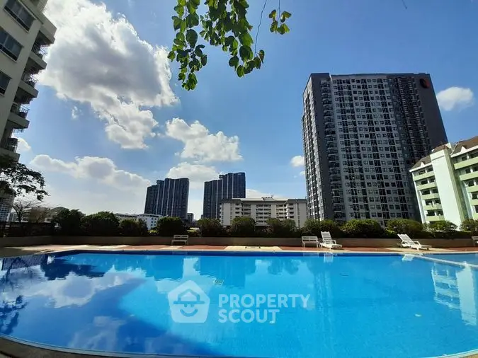 Inviting communal pool with crystal-clear waters, flanked by modern high-rise buildings under a bright blue sky, offering a serene urban oasis.