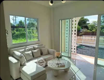 Bright living room with large windows and garden view, featuring a cozy white sofa and modern decor.