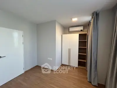 Spacious bedroom with wooden flooring and built-in wardrobe, featuring modern air conditioning unit.
