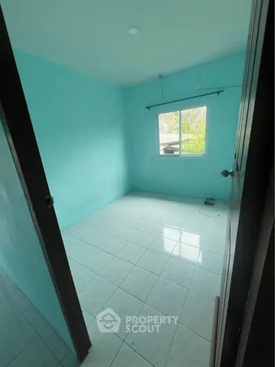 Bright empty room with turquoise walls and tiled floor, featuring a window with a view of greenery.