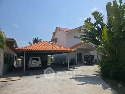 Charming suburban home with red-tiled roof, spacious driveway, and lush tropical landscaping.