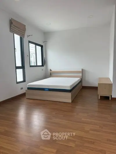 Spacious bedroom with wooden flooring and large windows for natural light.