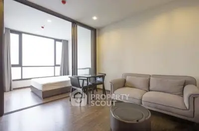 Modern apartment with open living room and bedroom, featuring sleek furniture and large windows.