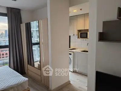Modern apartment interior with bedroom and compact kitchen, city view from window.