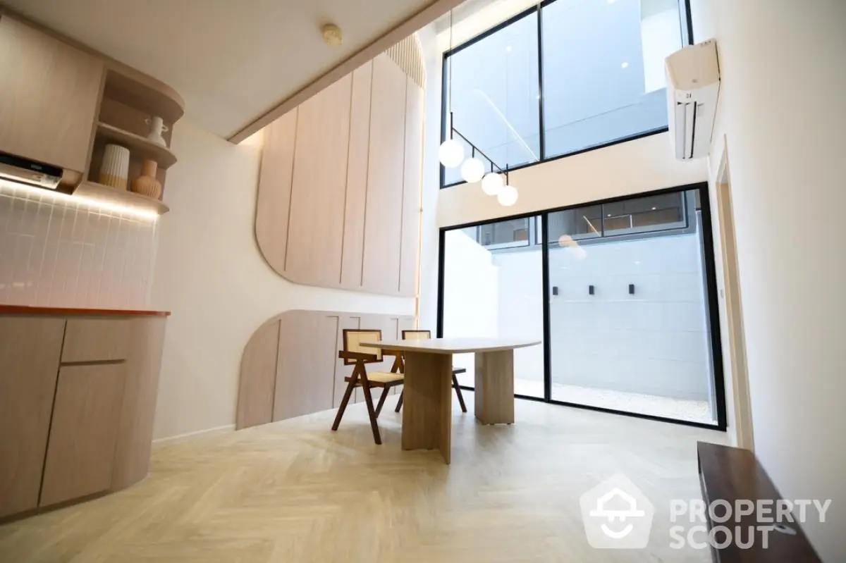 Modern dining area with high ceiling and large windows, featuring stylish wooden furniture and contemporary lighting.