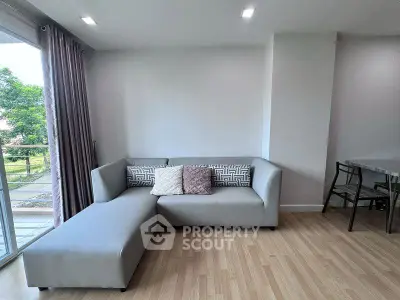 Modern living room with sleek gray sofa and wooden flooring, featuring a view of the balcony.