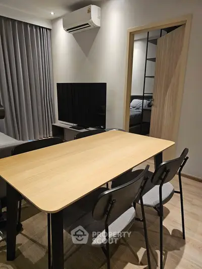 Modern dining area with sleek table and chairs, adjacent to a cozy living room with TV and air conditioning.