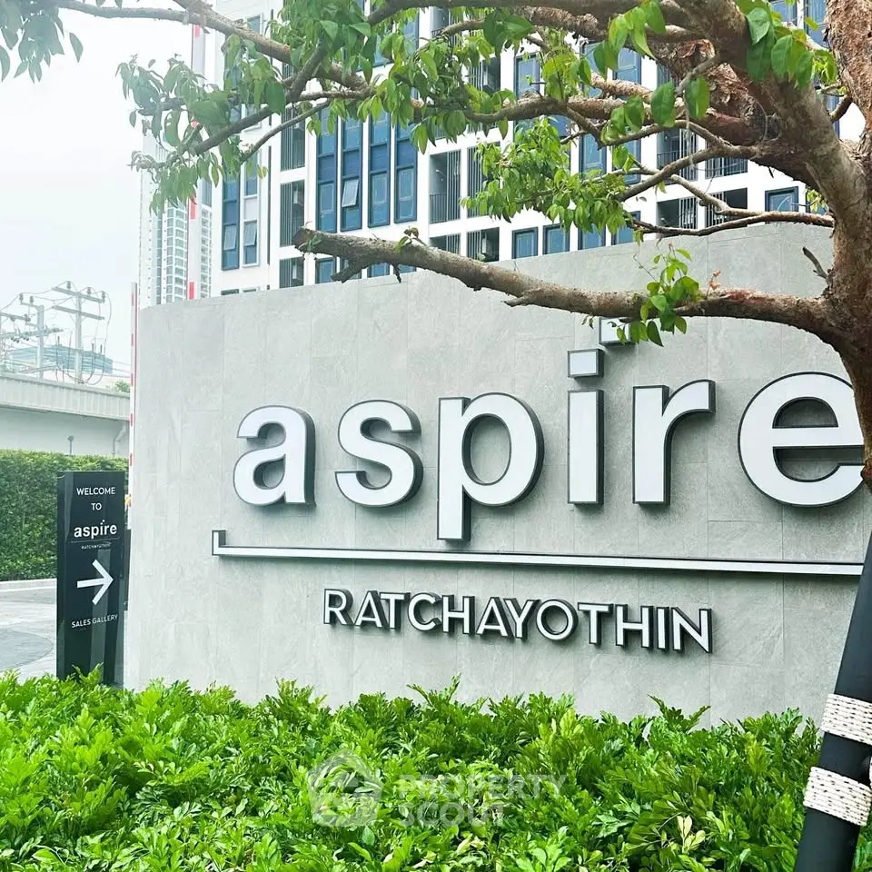 Modern Aspire Ratchayothin building entrance with lush greenery and sleek signage.