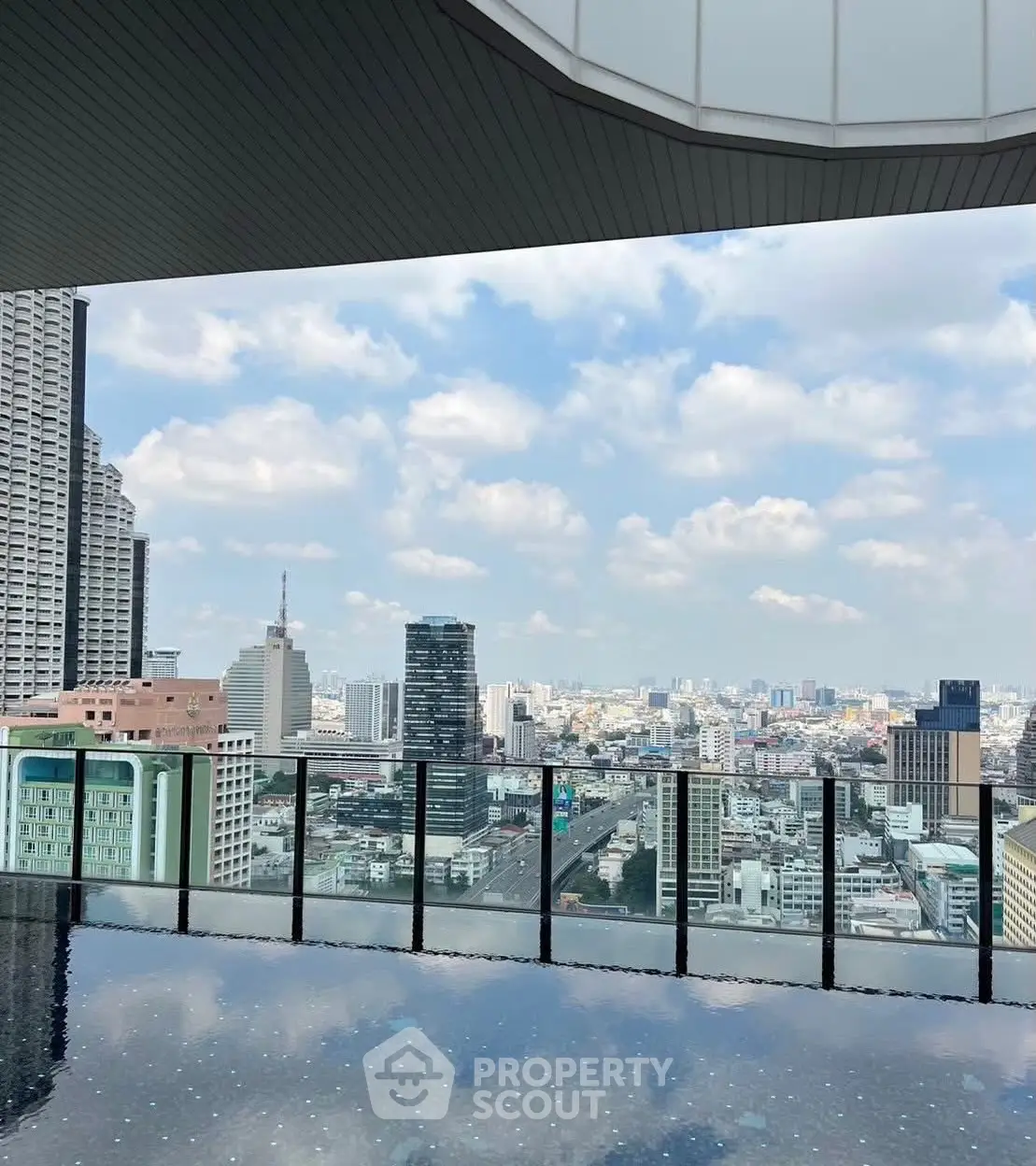 Stunning cityscape view from a modern high-rise balcony with glass railing and reflective flooring.