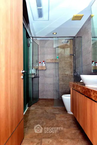 Modern bathroom with glass shower and wooden cabinetry in luxury home.