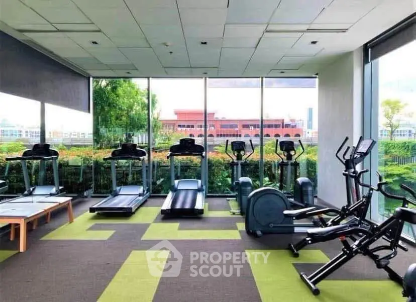 Modern gym with treadmills and exercise bikes in a bright, glass-walled space overlooking greenery.