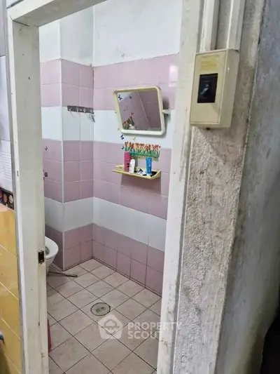 Charming pink-tiled bathroom with mirror and shelf, perfect for cozy living spaces.