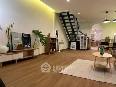 Spacious modern living room with wooden flooring and stylish decor, featuring a staircase and open layout.