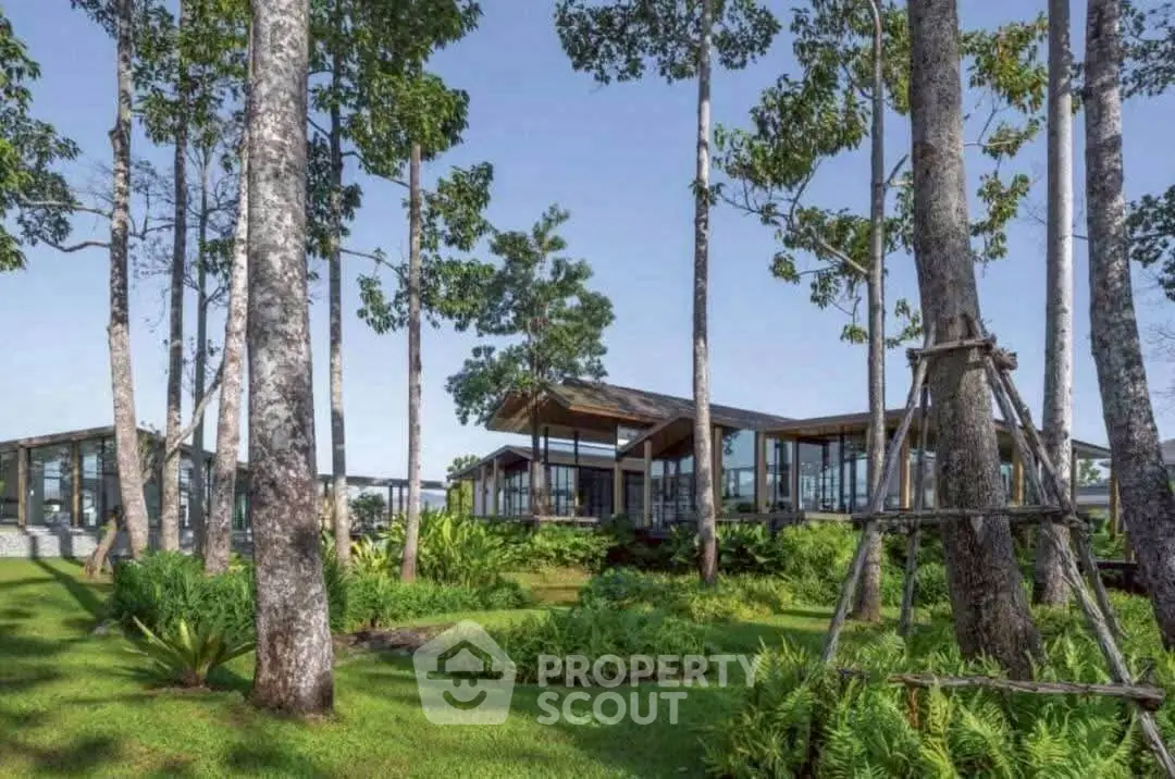 Stunning modern home with expansive glass windows surrounded by lush greenery and tall trees.