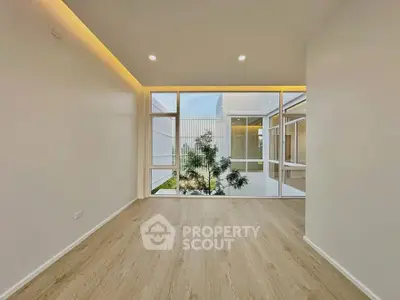 Spacious modern room with large windows and wooden flooring, offering a serene garden view.