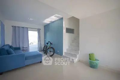 Spacious living room with modern blue sofa and staircase, featuring a bicycle and natural light.