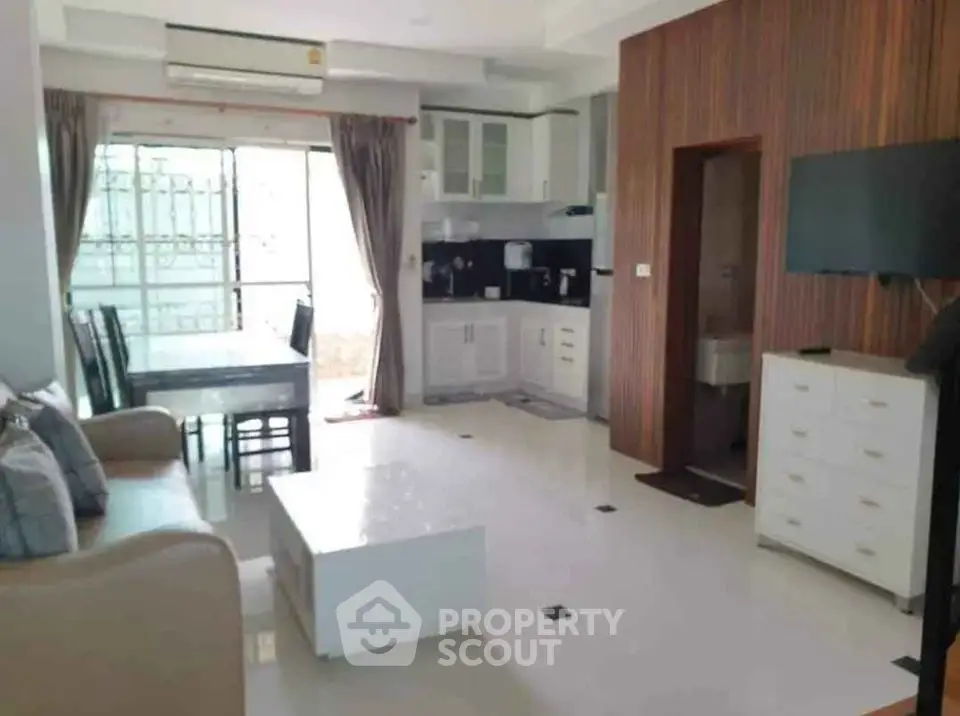 Modern open-layout living room with kitchen and dining area, featuring sleek furniture and ample natural light.