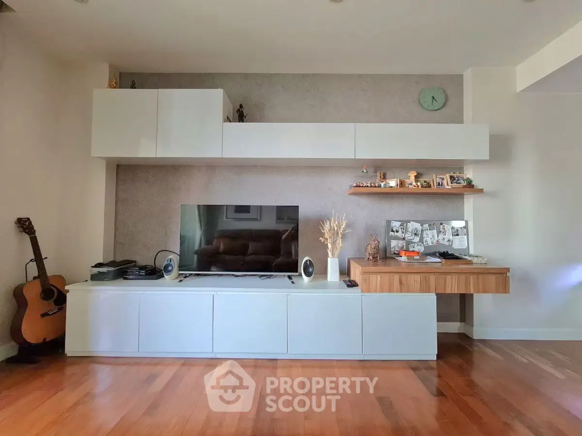 Modern living room with sleek white cabinets and wooden flooring, featuring a guitar and decorative items.